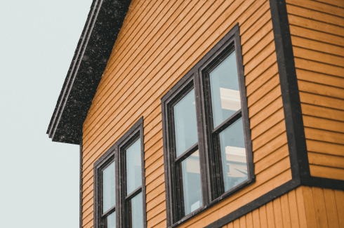 GRT Roofing keeps homes safe during snowy weather, as shown by a cozy yellow house with falling snow outside.
